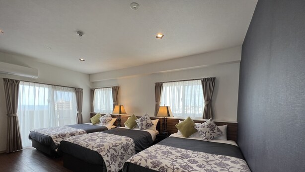 A hotel room with three beds, a large window with curtains, a wooden floor, and a ceiling with recessed lighting. - BiBi Hotel Convention Bay (Ginowan)