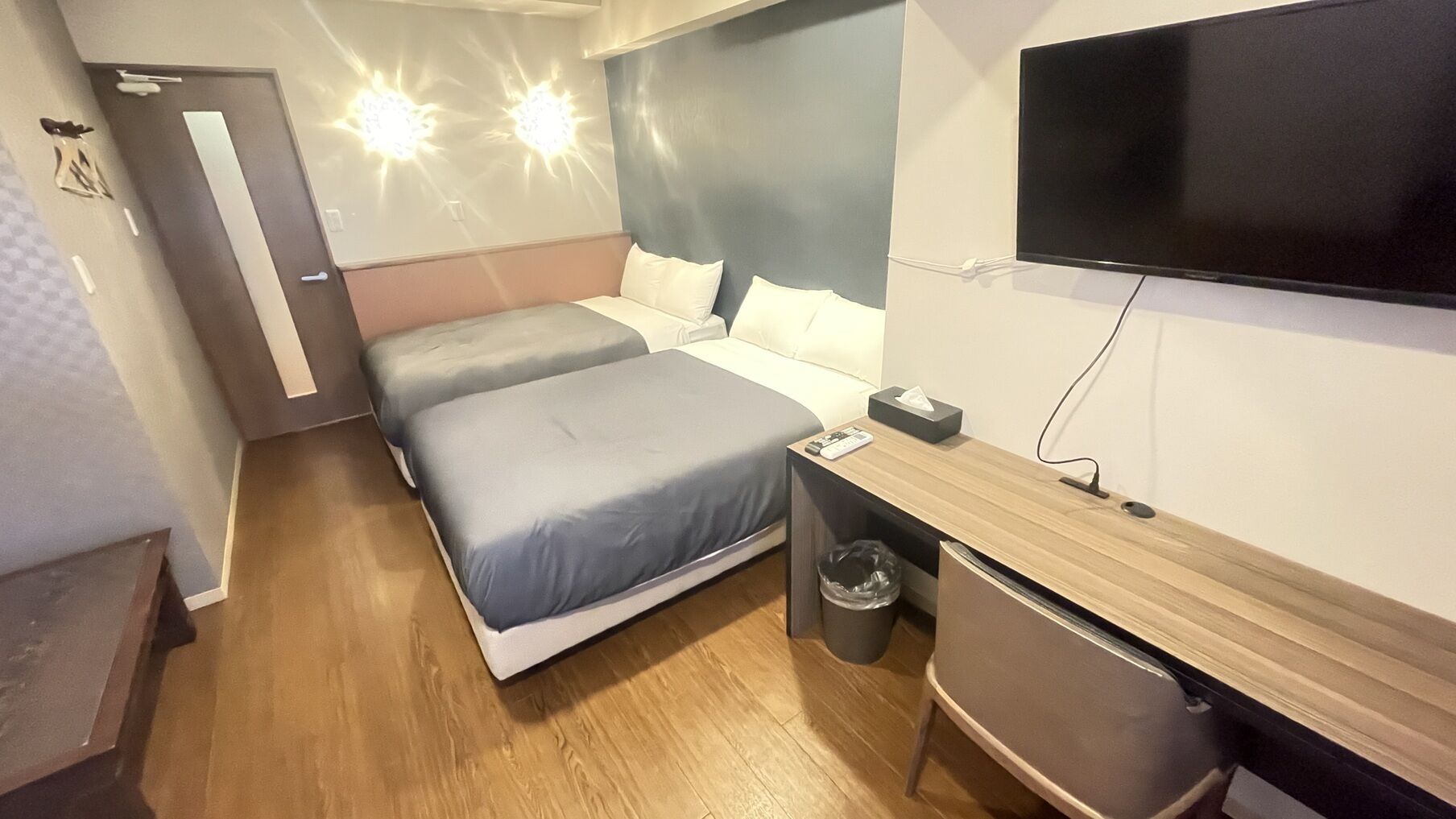 A hotel room with two beds, a desk, a television, and a trash bin.