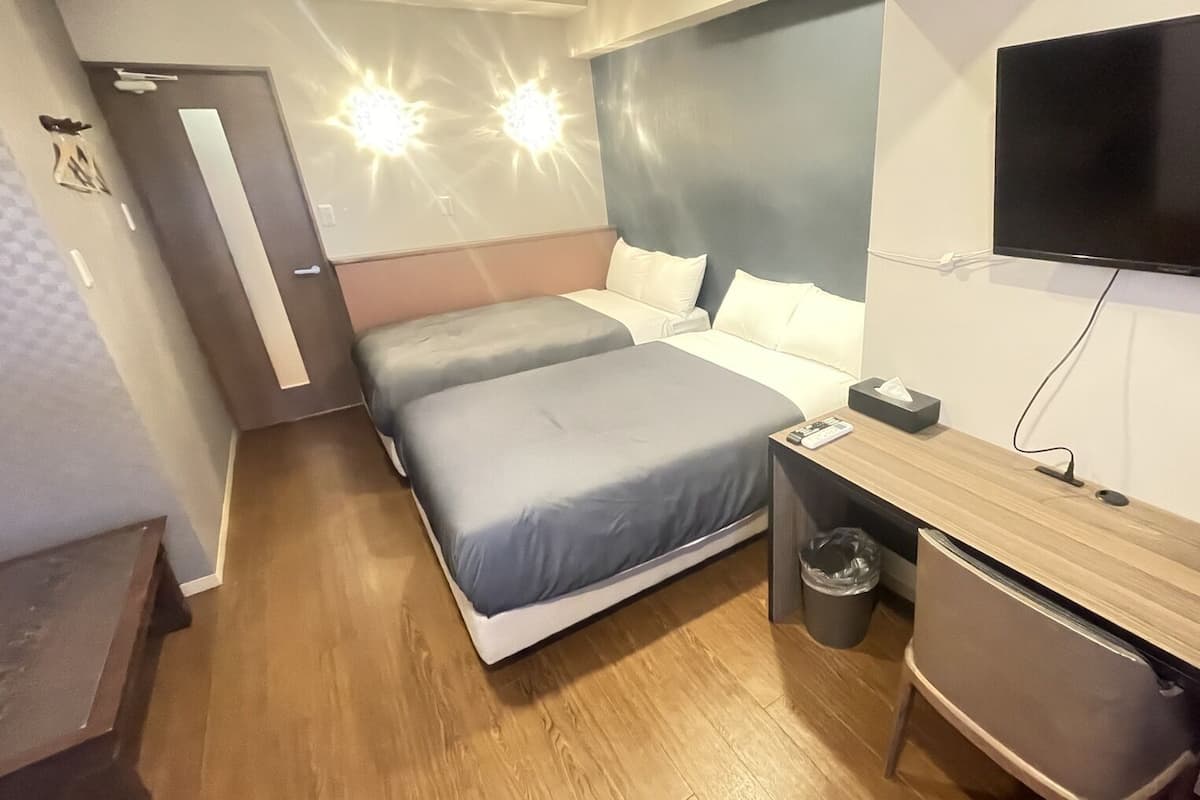 Ein Hotelzimmer mit zwei Betten, einem Schreibtisch, einem Fernseher und einem Mülleimer.
