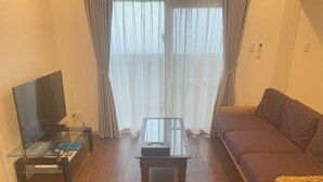 A living room with a flat-screen TV, a glass coffee table, a brown sofa, and a wicker chair. - BiBi Hotel Convention Bay (Ginowan)