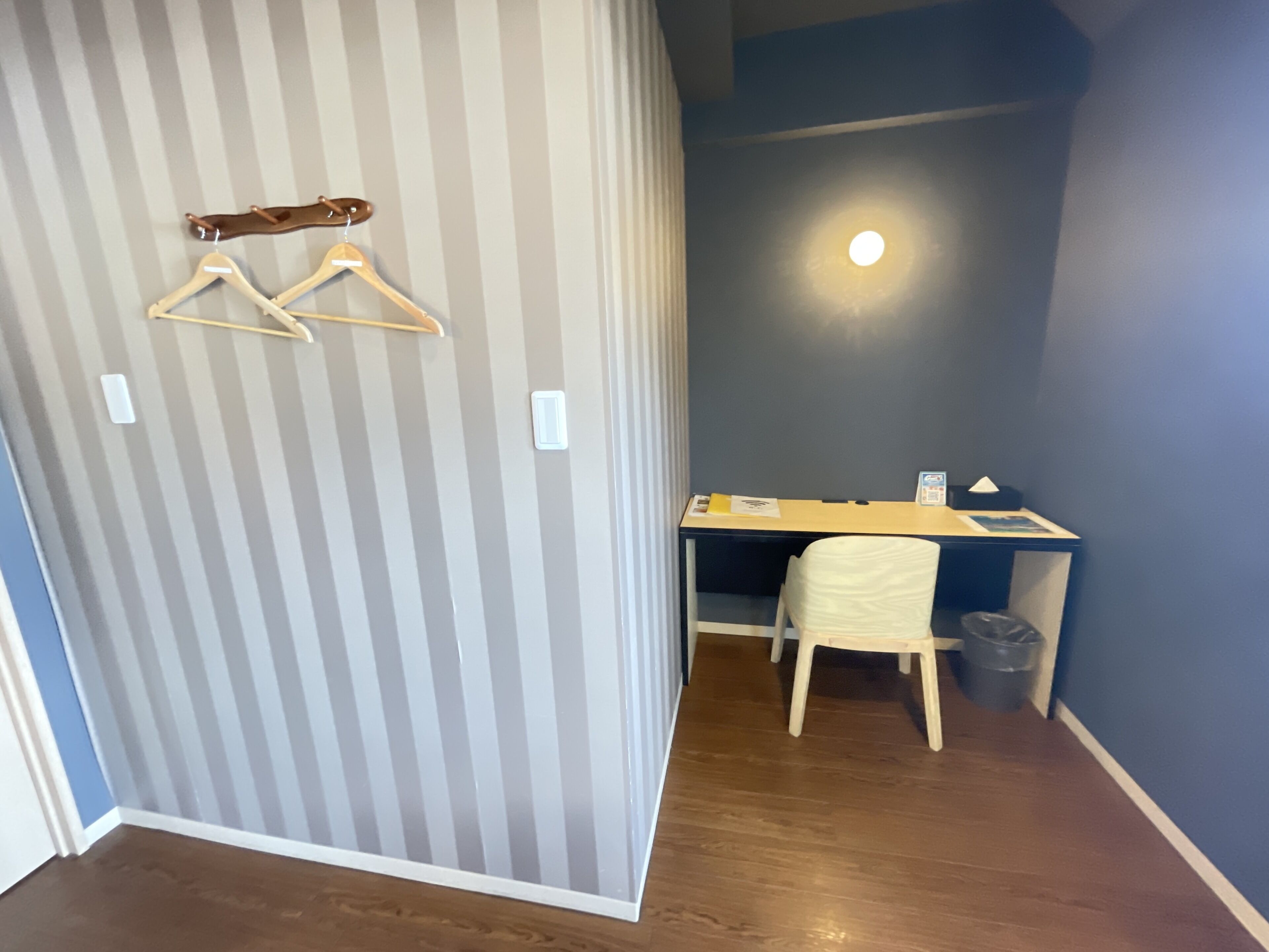 Ein Zimmer mit gestreifter Wand, einem Schreibtisch, einem Stuhl und einem hängenden Kleiderständer.