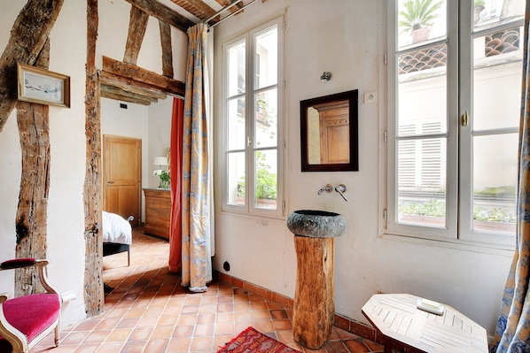 A rustic room with exposed wooden beams, a stone sink, a wooden cabinet, and a red chair.