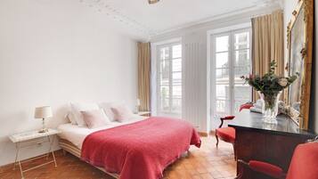 Une chambre d’hôtel comprenant un lit, une table de chevet, une chaise, une commode, un miroir et une fenêtre avec des rideaux.