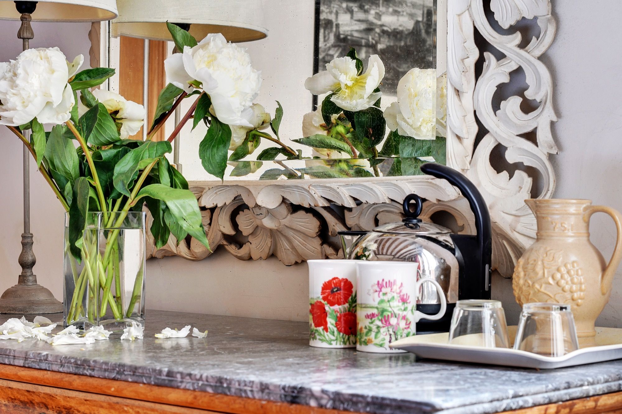 Un plan de travail en marbre orné d’un vase de fleurs blanches, d’une théière, d’un pichet et d’un plateau avec des tasses et des verres.
