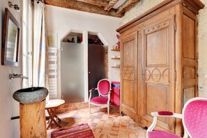 Una habitación con un armario de madera, una silla roja, una mesita pequeña y suelo de baldosas.
