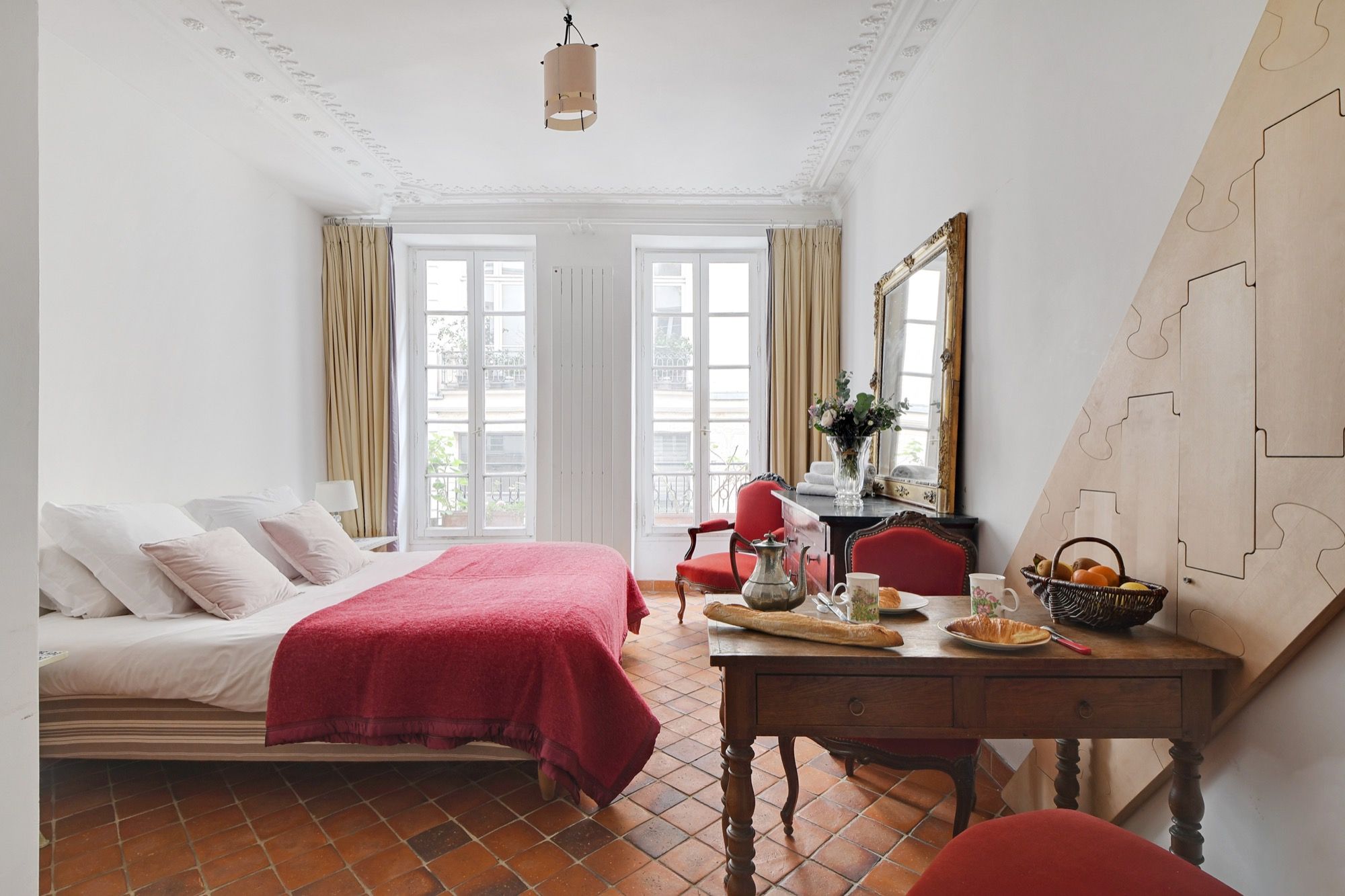 A hotel room with a bed, a desk with a vase, a mirror, and a window with curtains.