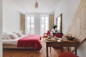 Una habitación de hotel con cama, escritorio con un florero, espejo y ventana con cortinas.