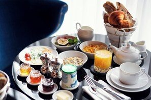 Bandeja de café da manhã com croissants, cereais, frutas e um copo de suco de laranja.