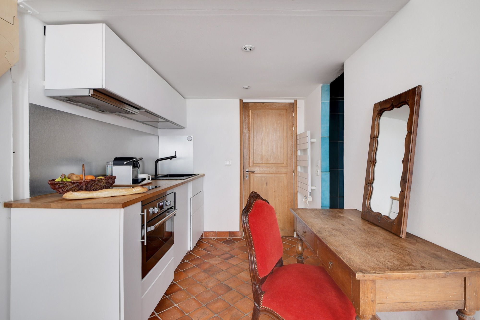 Een kleine keuken met een houten aanrecht, een rode stoel en een houten eettafel.