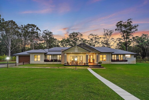 A modern two-story house with a well-maintained lawn, a driveway, and a porch with outdoor seating.