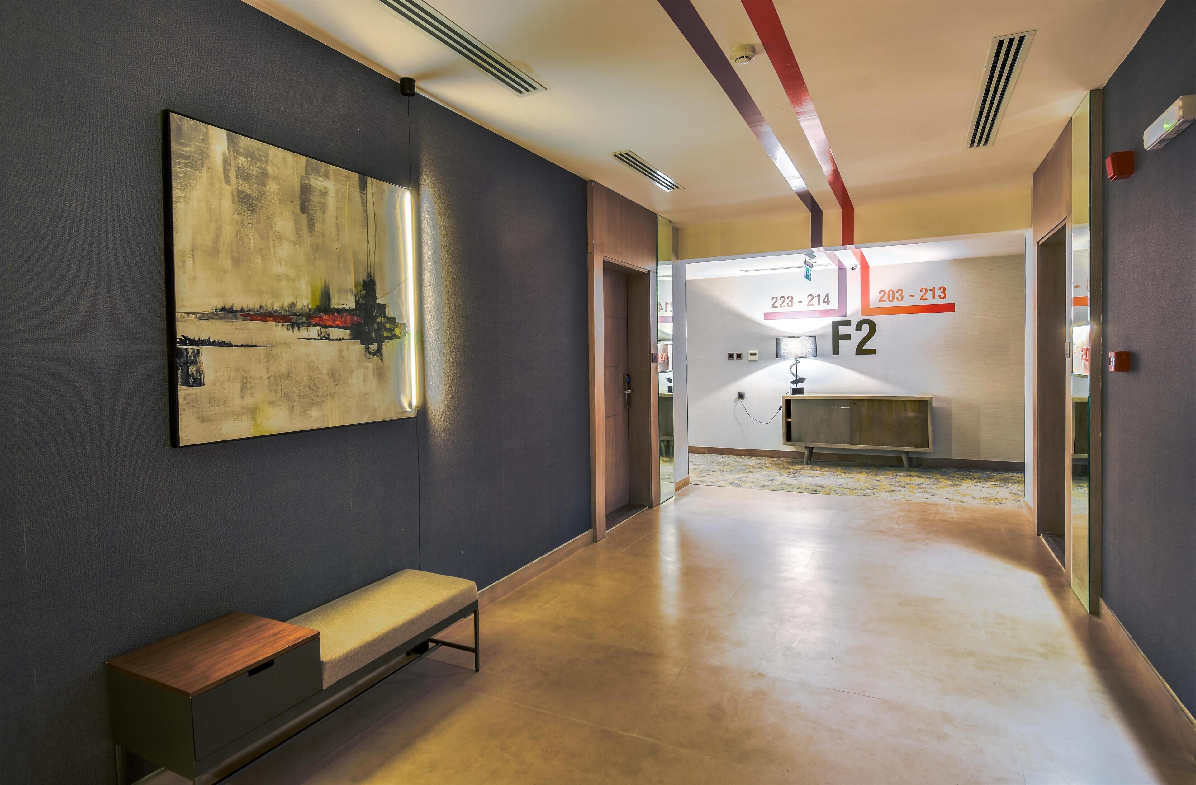 Un corridoio moderno di un hotel con una panca, un grande quadro astratto e un'area reception con porte numerate.