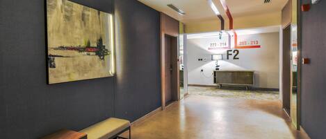 Un corridoio moderno di un hotel con una panca, un grande quadro astratto e un'area reception con porte numerate.