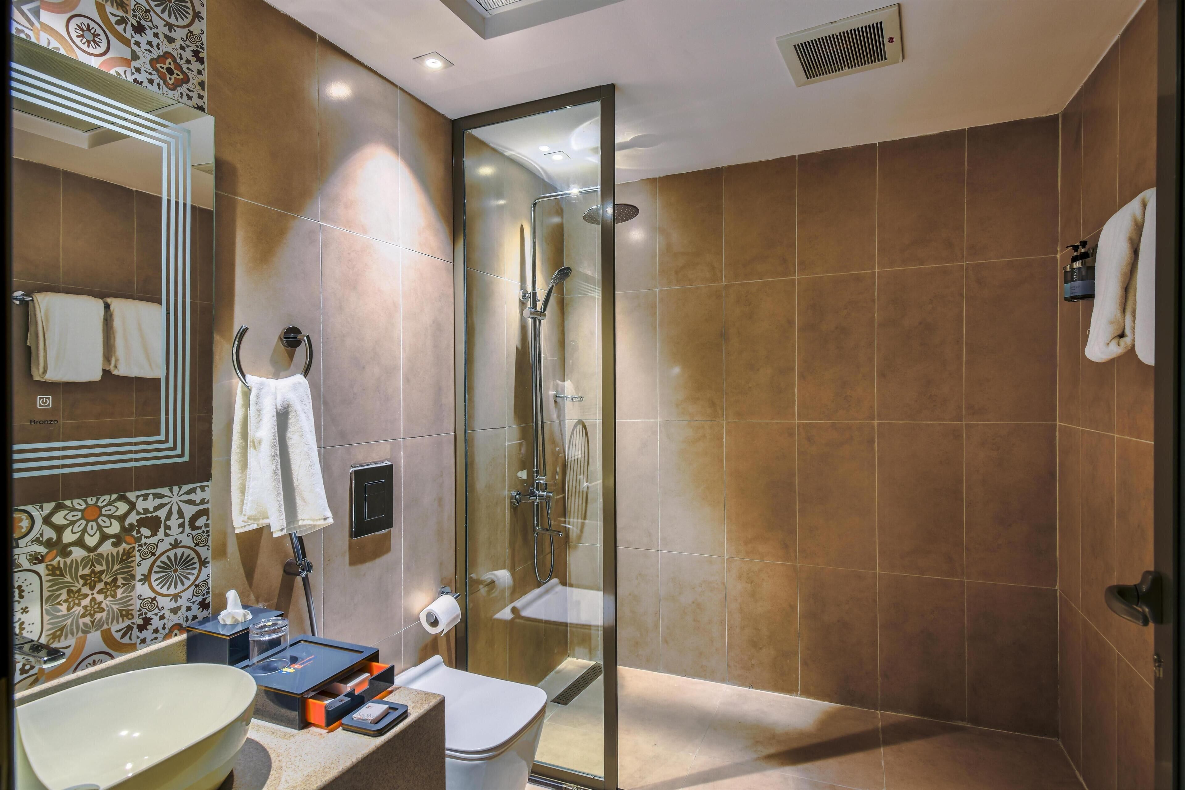 A modern bathroom with a glass-enclosed shower, a toilet, and a sink with a mirror above it.