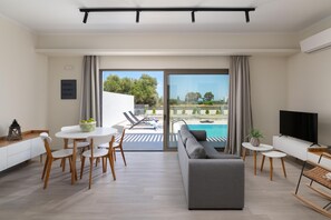 A modern living room with a sofa, dining table, chairs, a TV, and a pool view.