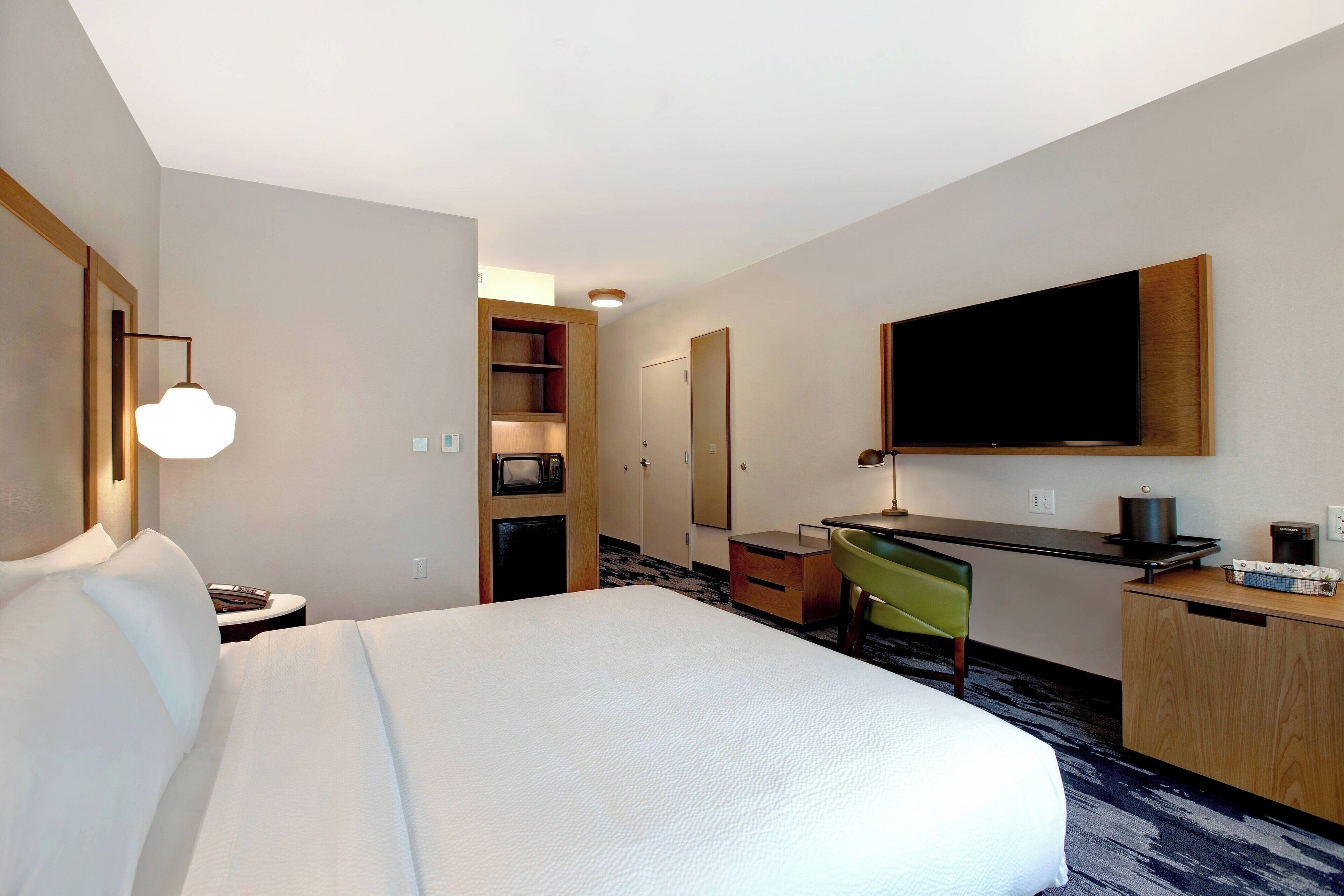 A hotel room with a bed, desk, chair, TV, and a minibar.