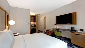 A hotel room with a bed, desk, chair, TV, and a minibar.