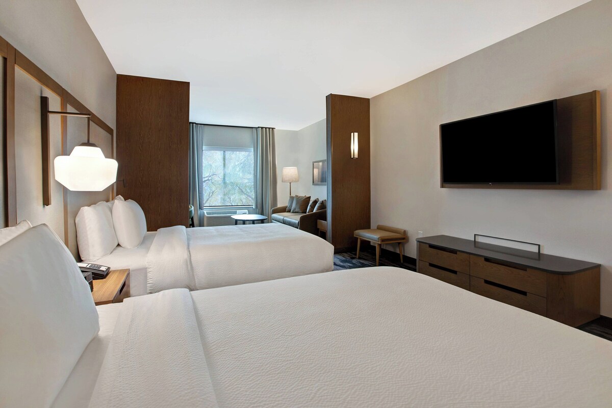 A hotel room with two beds, a TV, a desk, and a window with a view.