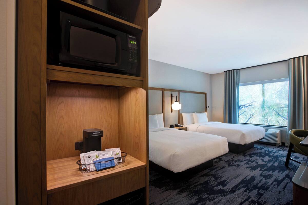 A hotel room with two beds, a microwave, a coffee maker, and a window with a view.