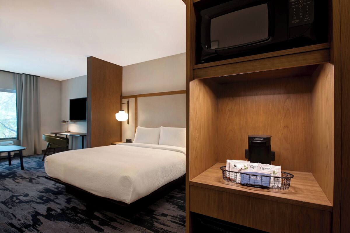 A hotel room with a bed, a desk, a television, a microwave, and a basket with toiletries.