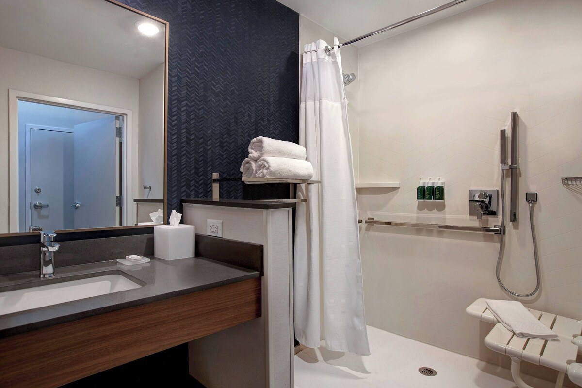 A modern bathroom with a large mirror, a sink, a shower with a glass door, and a toilet.