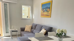 Una sala moderna con un sofá gris, una mesa de comedor con individuales y un florero con flores.