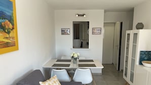 Una sala moderna con un sofá gris, una mesita con un jarrón de flores y un comedor con una mesa y sillas blancas.