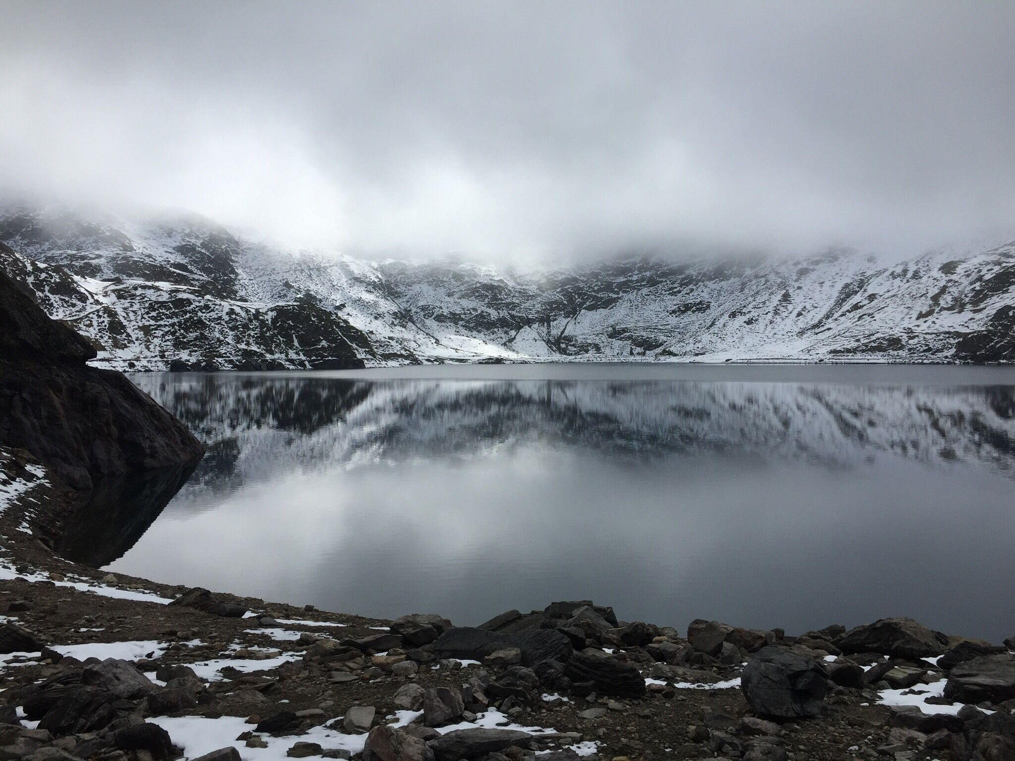 Ein stiller See, umgeben von schneebedeckten Bergen und felsigem Gelände.