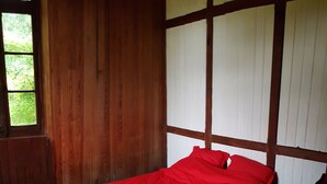 Une pièce avec un plancher en bois, un lit recouvert d’une courtepointe rouge et une fenêtre donnant sur un paysage verdoyant.