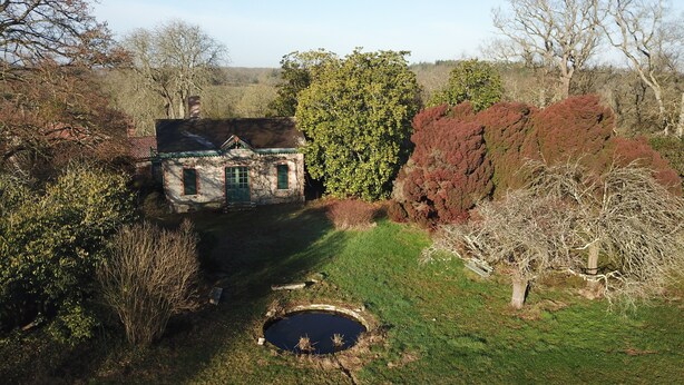 Une maison de campagne en pierre, avec une porte verte, entourée d’un jardin bien entretenu et agrémentée d’un petit étang.