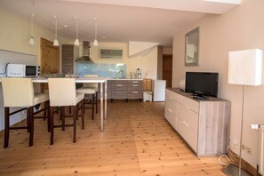 Eine moderne Küche mit Holzboden, einem Essbereich mit Stühlen, einem Fernseher und einer Lampe.