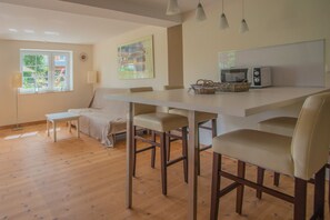 Eine moderne Küche mit weißer Arbeitsplatte, einer Mikrowelle und einem Korb. Ein Fenster bietet Blick ins Grüne.
