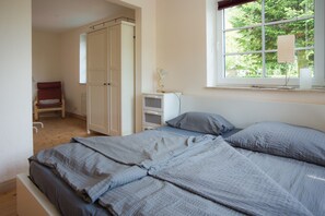 Ein Schlafzimmer mit Bett, Stuhl, Kleiderschrank, Nachttisch und einem Fenster mit Blick ins Grüne.
