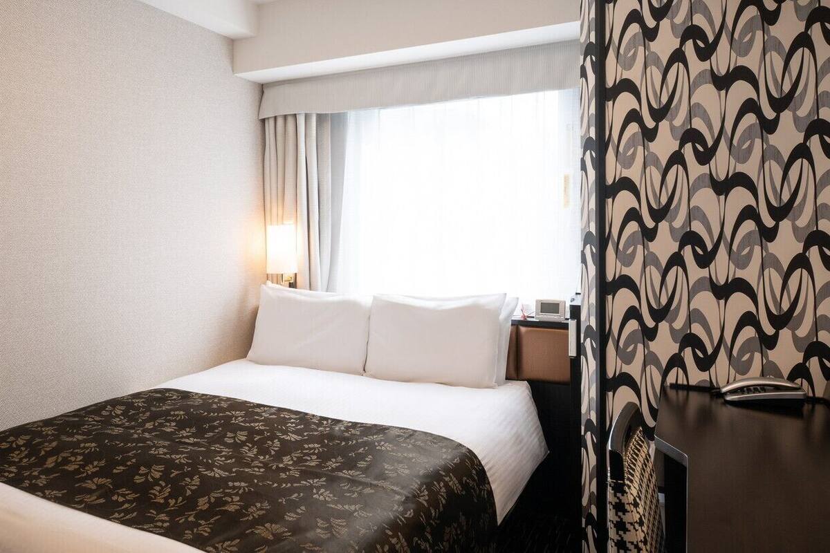 A hotel room with a bed, a nightstand, a lamp, and a patterned curtain.