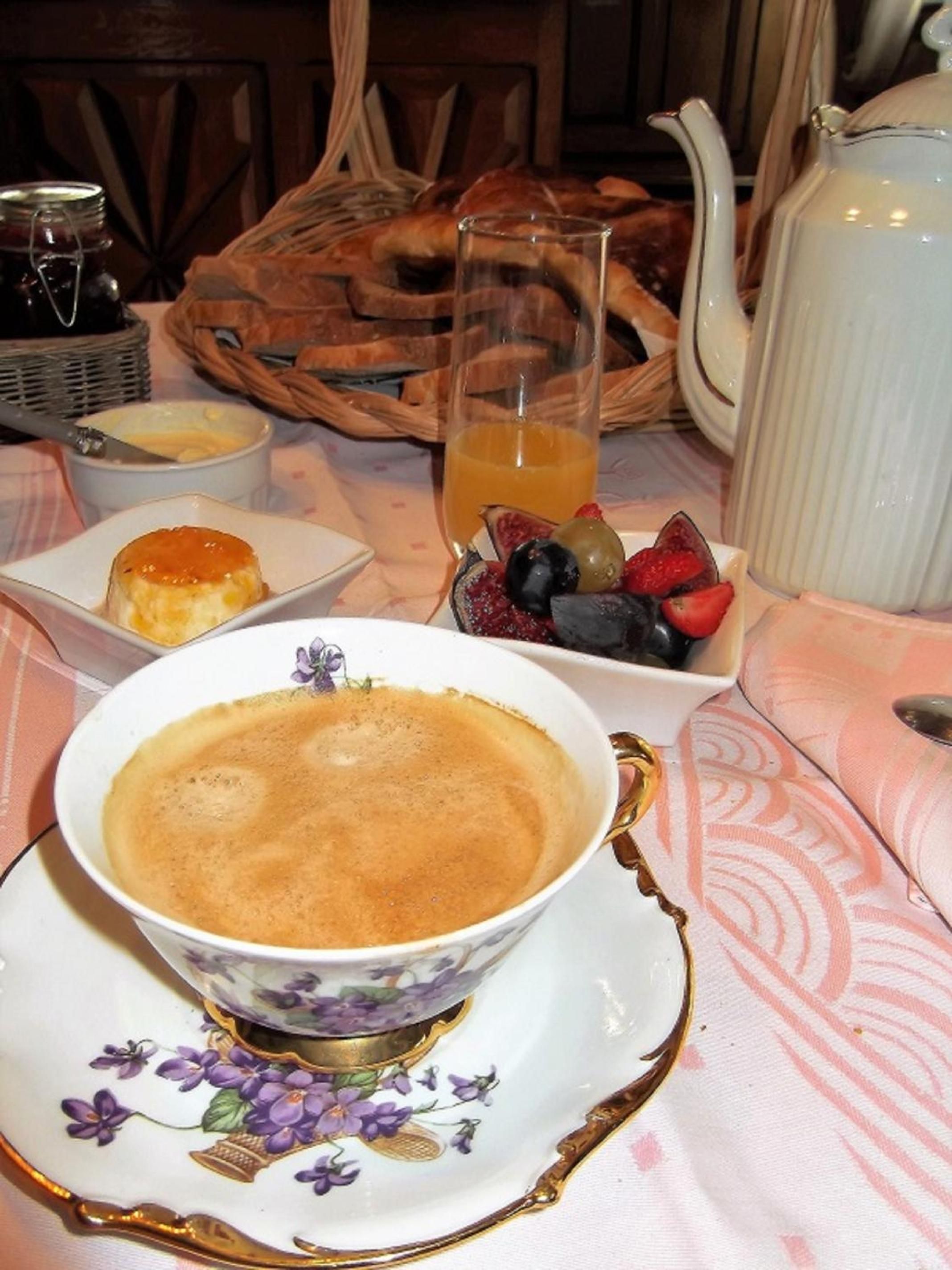 Una mesa servida con una taza de café, un cuenco de fruta y una tetera.