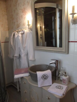 Ein Badezimmer mit einem großen Spiegel, einem Steinsink und einem Handtuchhalter mit Bademänteln.