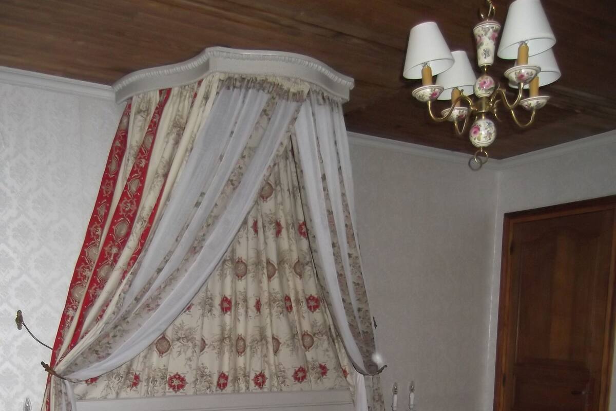 Une chambre à coucher avec un lit à baldaquin, une literie à motifs floraux, un plancher en bois et un lustre.