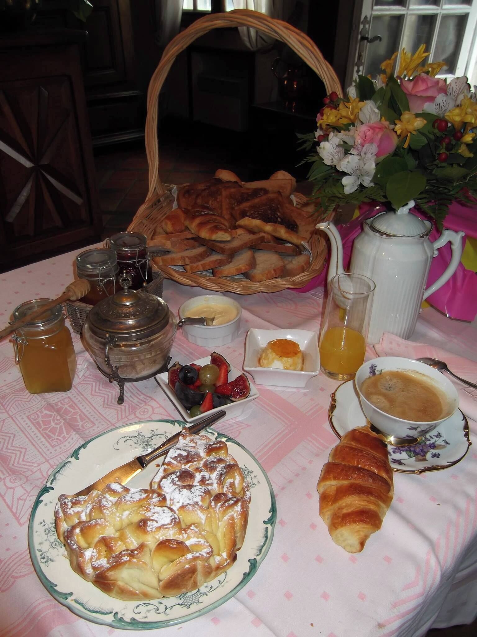 Une table de petit-déjeuner avec du pain, des viennoiseries, des fruits, du miel, de la confiture et du café.