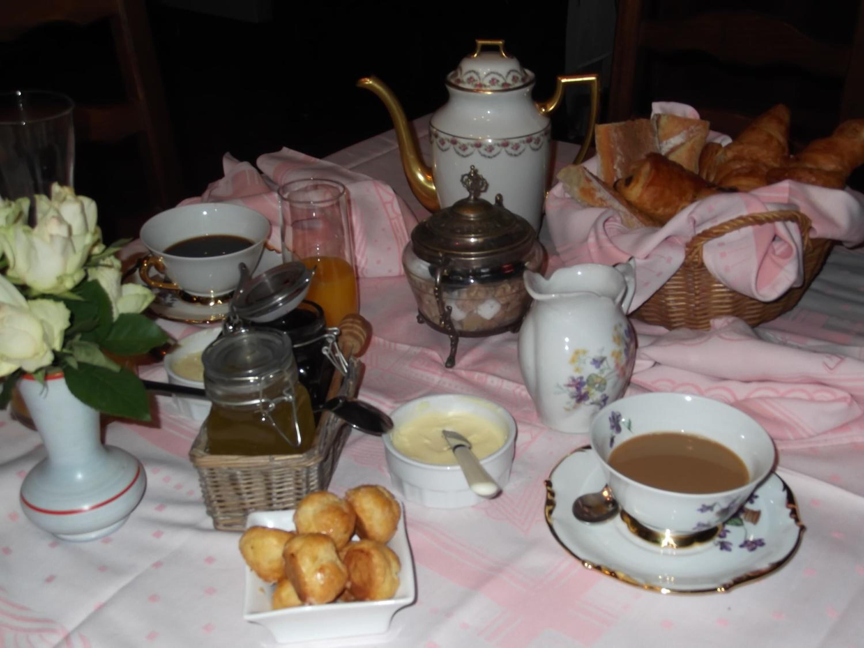Une table dressée avec du thé, du café, des pâtisseries et un vase de fleurs.