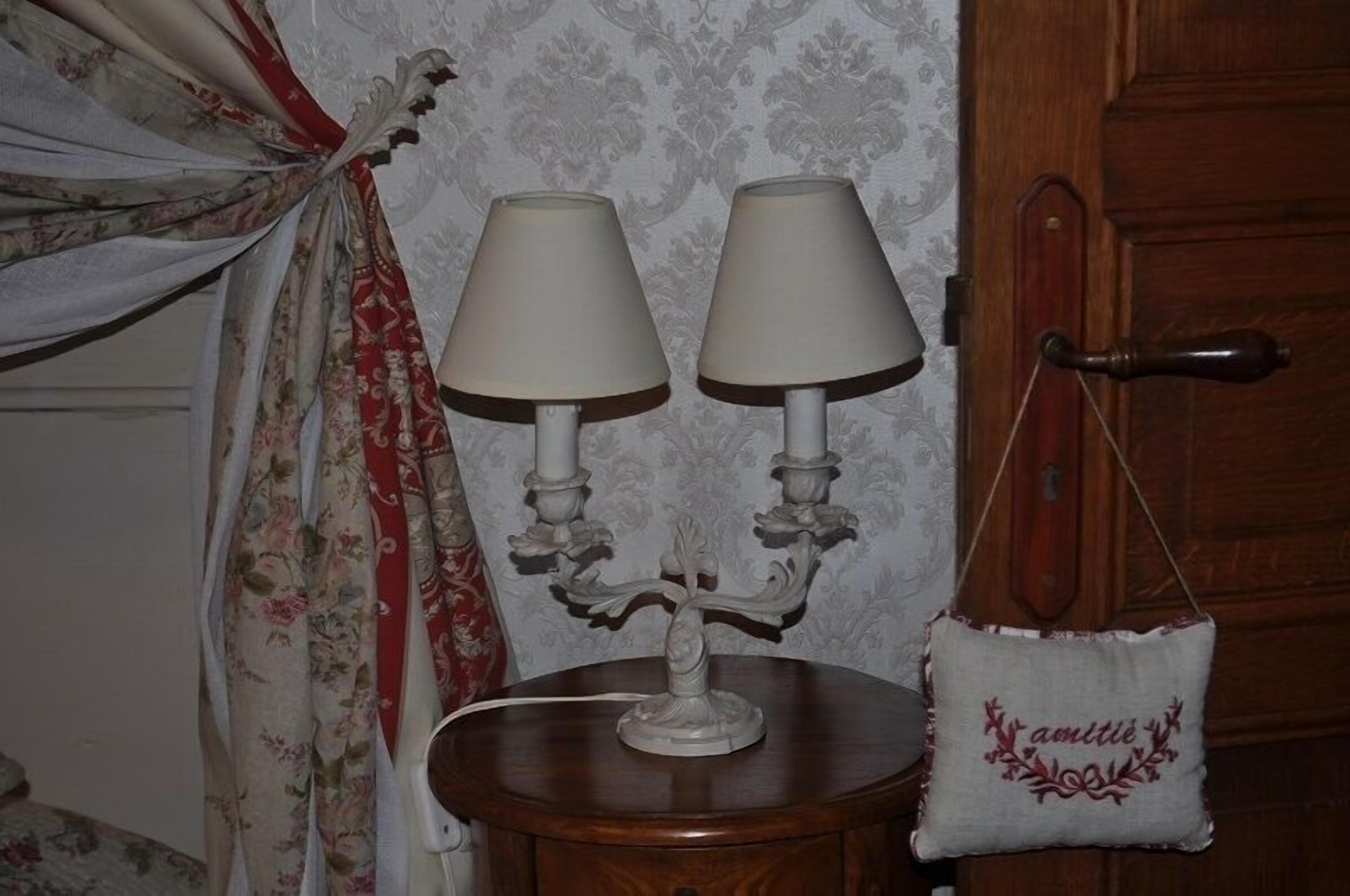 Une pièce avec une porte en bois, une petite table ronde surmontée de deux lampes blanches et un rideau à motifs floraux.