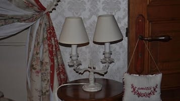 Une pièce avec une porte en bois, une petite table ronde surmontée de deux lampes blanches et un rideau à motifs floraux.