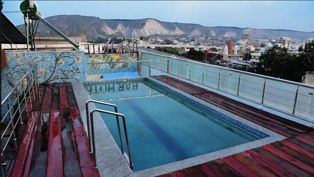 A rooftop swimming pool with a view of a cityscape and mountains in the background. - Broadway Inn (Jaipur)