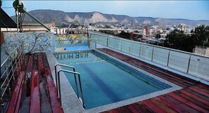 Una piscina en la azotea con vistas a un paisaje urbano y montañas al fondo.