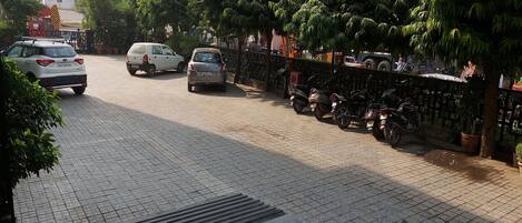 A paved street with parked cars and motorcycles, trees, and a fence.