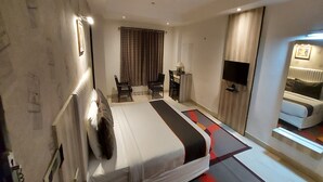 A hotel room with a bed, a desk, a chair, a TV, and a sofa. - Broadway Inn (Jaipur)