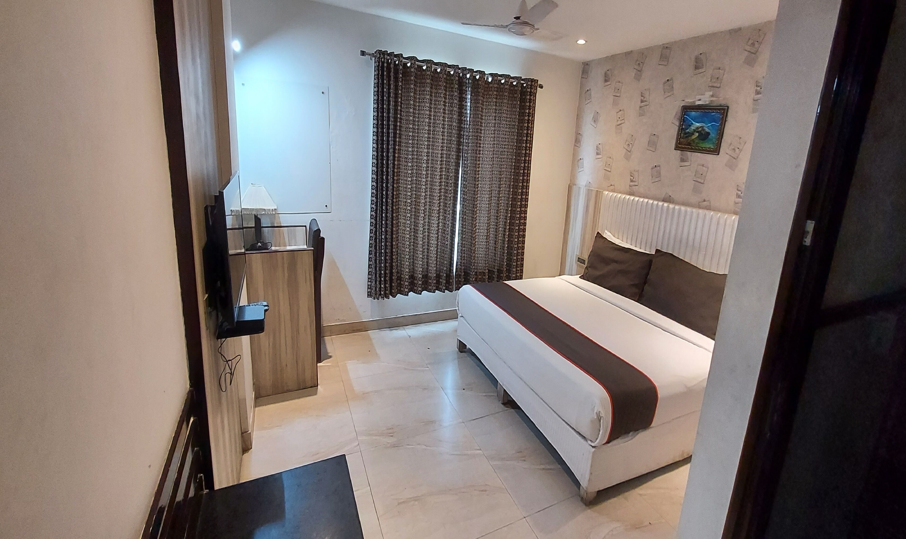 A bedroom with a bed, a desk, a chair, a window with curtains, and a wall with pictures.
