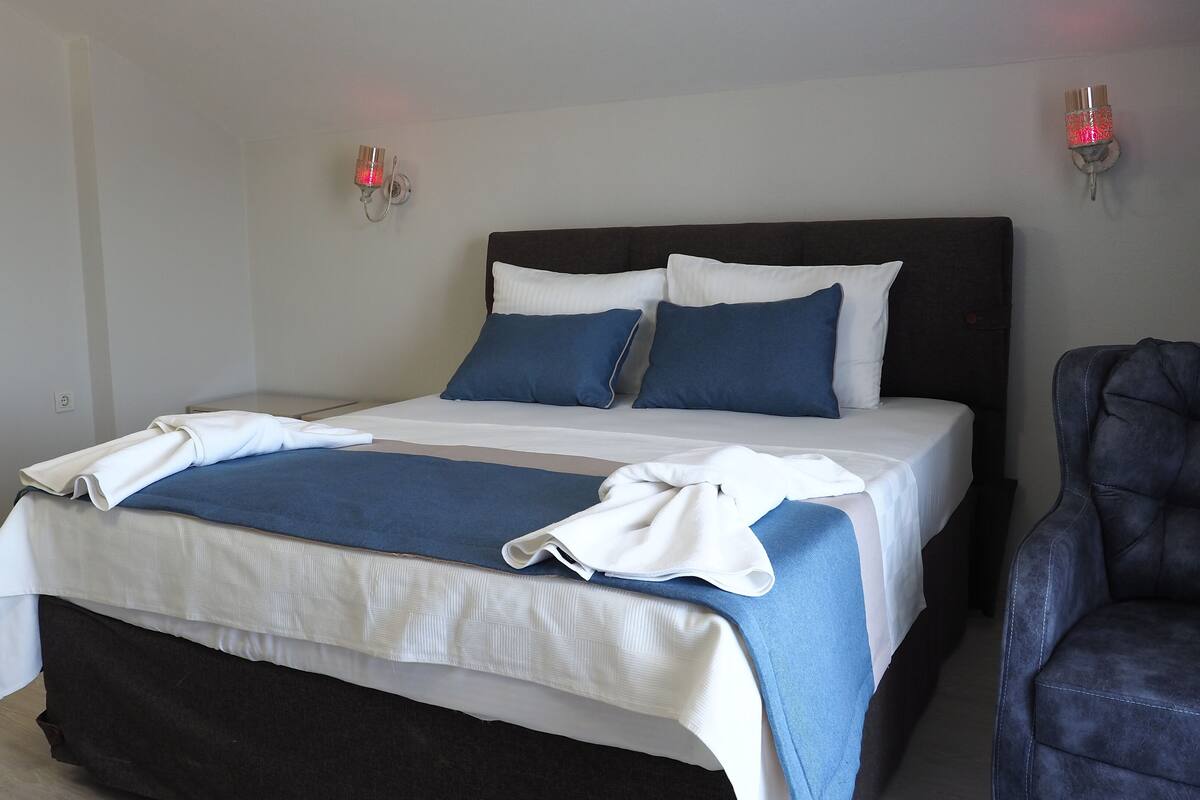 Ein ordentlich bezogenes Bett mit weißer und blauer Bettwäsche, ein dunkles Kopfteil und zwei Wandleuchten.