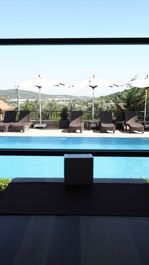 A poolside area with lounge chairs and umbrellas, a view of the pool, and a distant landscape.