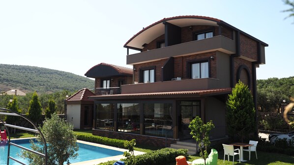 A modern two-story house with a swimming pool, a covered patio, and a view of a hilly landscape. - Myosotis Boutique Otel (Foça)