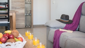 Uma sala de estar moderna com um sofá cinzento, uma mesa de jantar de madeira com frutas e sumo de laranja, e um chapéu no sofá.