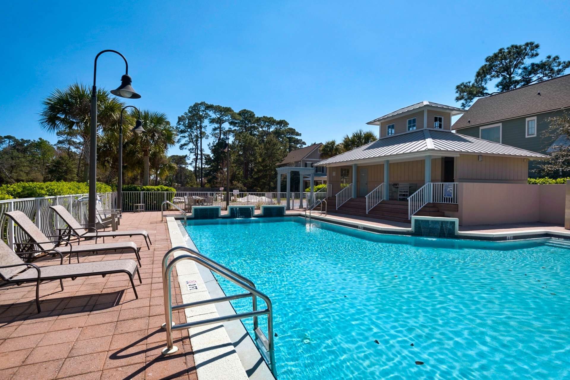 A swimming pool with a clear blue water, surrounded by a deck with lounge chairs and a pergola.
